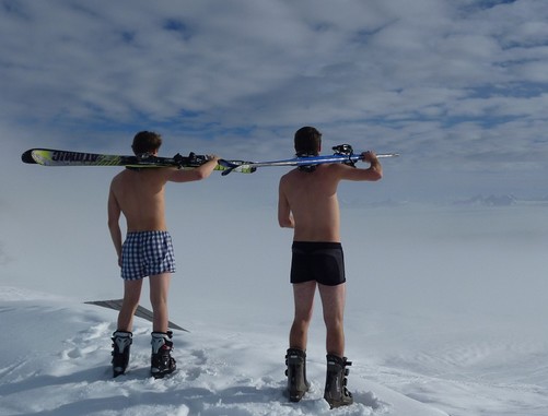 Két férfi hátulról alsónadrágban, sícipőben, vállukon sítalpak, így nézik a havas tájat, Kép: pixabay  