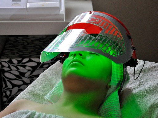 Kozmetikai ágyon fekvő nő, fején egy hokis fejvédőjéhez hasonló, zöld-piros álarc, Kép: Aranyalma Szépségszalon