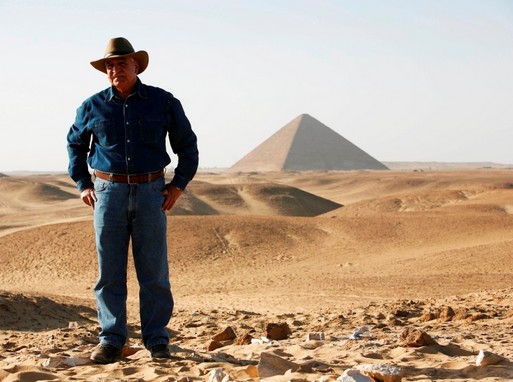 Az egyiptomi kutató zsebre dugott kézzel, mögötte egy piramis, Kép: Do-Q