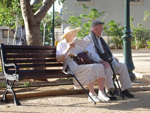 Nyugdíjas idős pár ül egy kerti padon, a hölgy újságot olvas, Kép: pixabay 