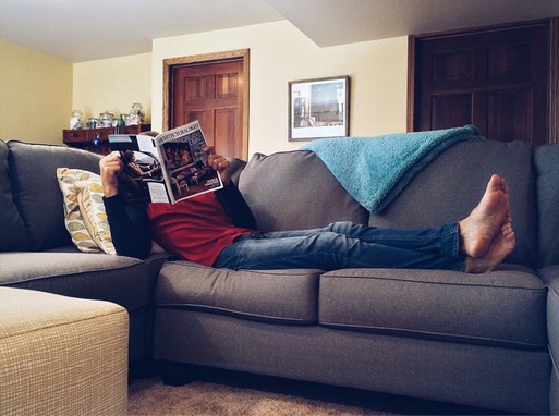 Lakásban, heverőn fekvő férfi újságot olvas, Kép: pexels